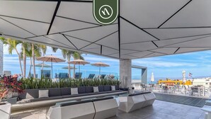 A rooftop lounge with a pool, outdoor seating, and a view of the ocean.