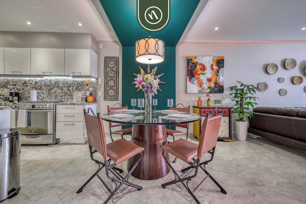 A modern kitchen with white cabinets, a marble backsplash, and a dining area with a glass table and leather chairs.