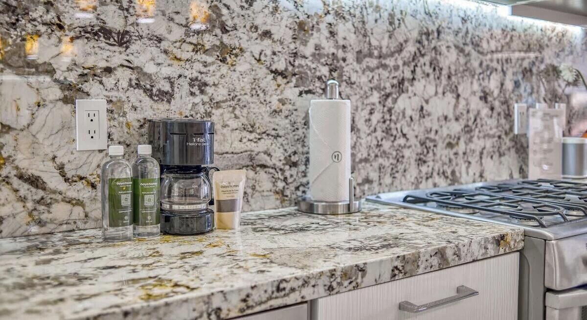 A kitchen with a marble countertop, a coffee maker, a kettle, and a range hood.