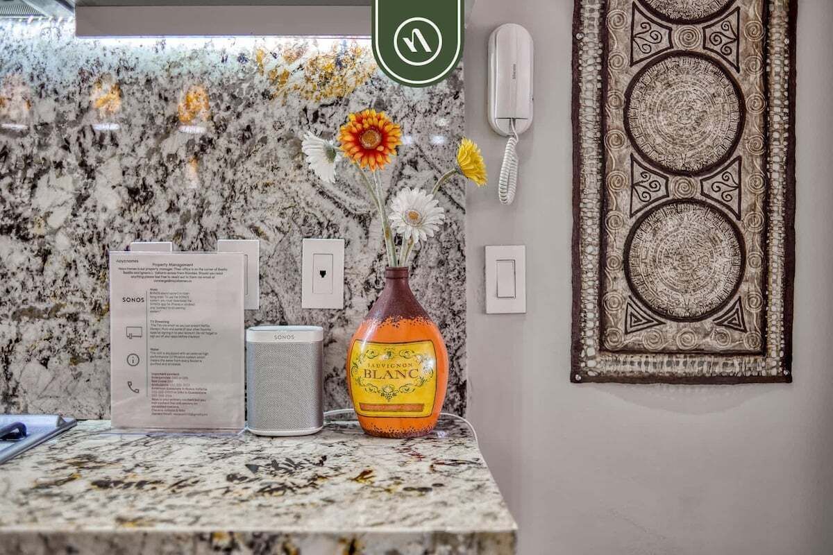 A marble countertop with a vase of flowers, a phone, a speaker, and a menu.