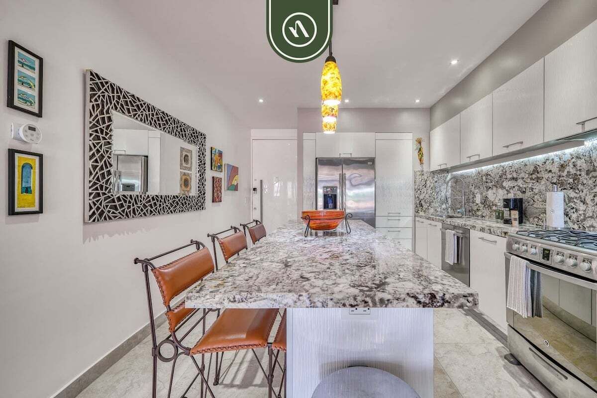 A modern kitchen with a marble countertop, stainless steel appliances, and a dining area with leather chairs.