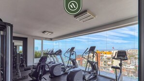 A gym with cardio machines, weight equipment, and a large window with a city view.