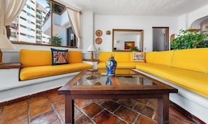 Una sala de estar con sofás amarillos, una mesa de centro de cristal y un espejo grande.