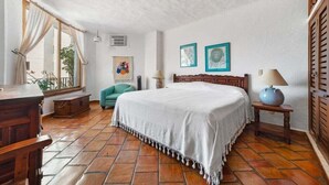 Un dormitorio con cama, escritorio, silla, ventana con cortinas y una pared decorada con dos cuadros.