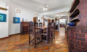 Un comedor amplio con techo alto, una cocina al fondo y suelo de baldosas.