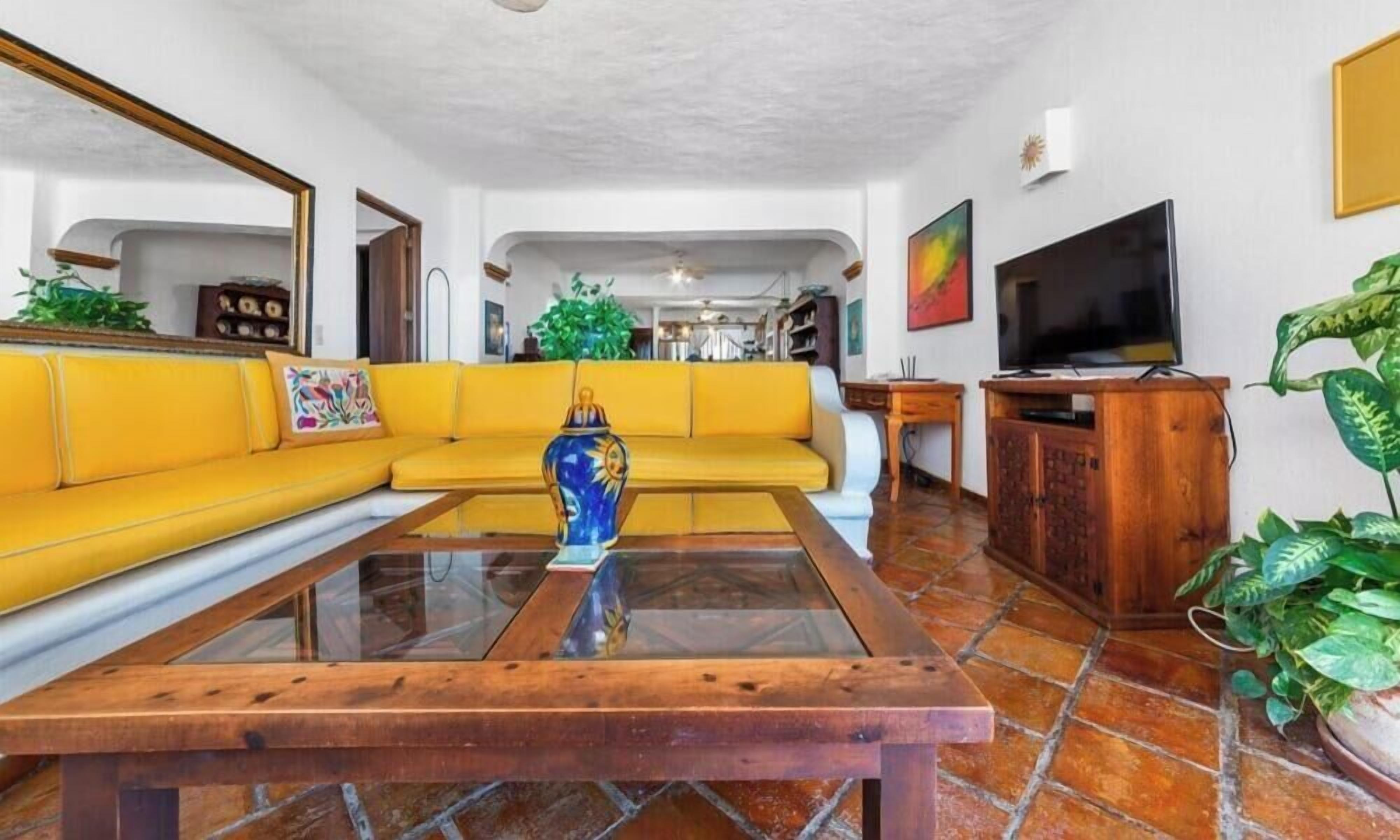 Un soggiorno con un divano giallo, un tavolino da caffè, una televisione e un mobiletto in legno.