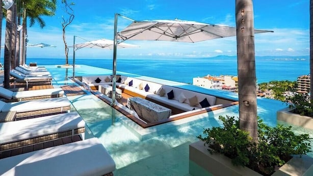 A poolside area with lounge chairs, umbrellas, and a view of the ocean. - Luxury 1 BR Condo in Pier 57 - Infinity Pool (Puerto Vallarta)