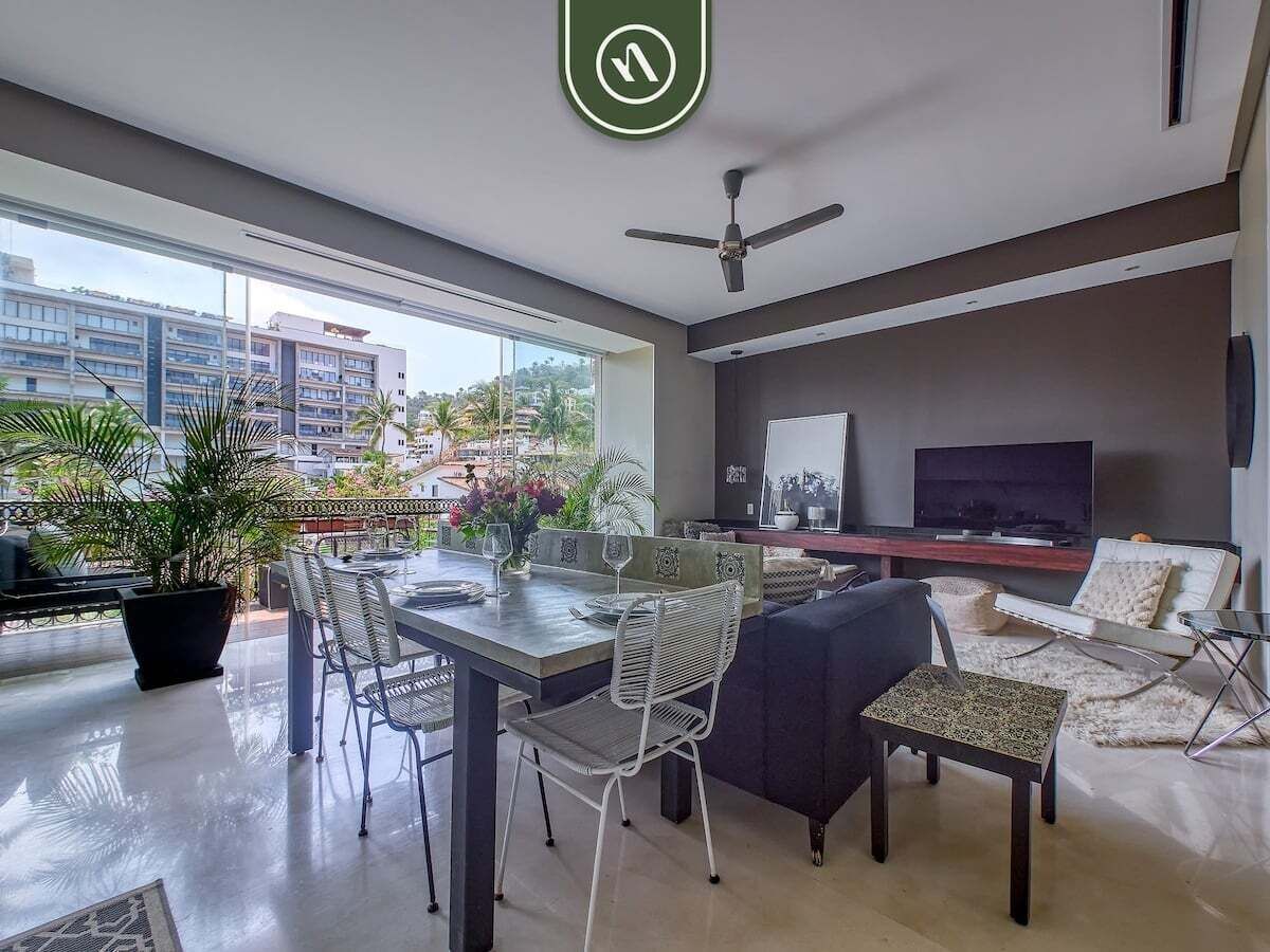 A modern living room with a dining area, a ceiling fan, a flat-screen TV, and a balcony with plants.