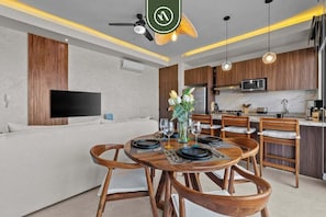 A modern kitchen with wooden cabinets, a built-in microwave, and a dining area with wooden chairs and a round table set for four.