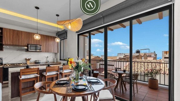 A modern kitchen with a dining area, large windows, and a view of the cityscape.