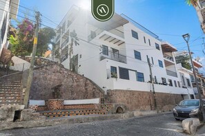 Un edificio de varios pisos con fachada blanca, una escalera de piedra y un coche estacionado.