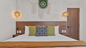 A hotel room with a wooden headboard, a bed with white bedding, two bedside tables, and two wall-mounted lamps.