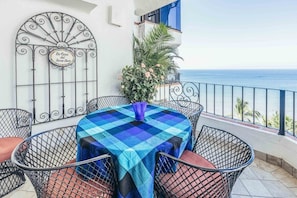 A balcony with a checkered tablecloth, metal chairs, a decorative metal gate, and a view of the sea. - Ocean View 2Br Condo-balcony-beach-pool - 805 (Puerto Vallarta)
