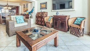 Un vaste espace de vie agrémenté de meubles en osier, d’une table basse en verre et d’un grand téléviseur à écran plat.