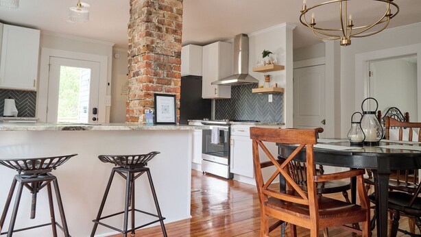 A modern kitchen with a brick column, white cabinetry, and a central island with bar stools.