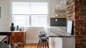 A kitchen with a large window, a wooden dining table, and a bar area with stools.