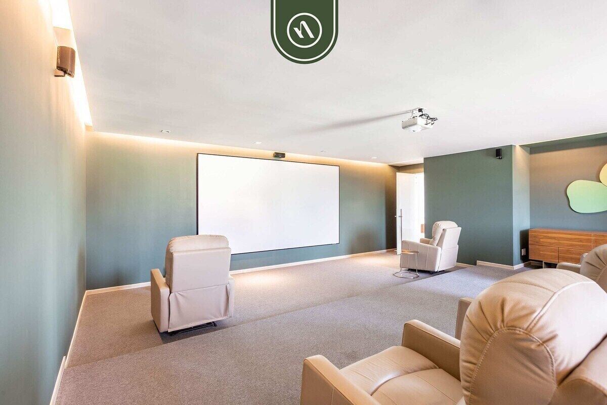 A room with a large screen, two white chairs, a wooden cabinet, and a ceiling-mounted projector.
