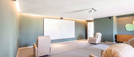 A room with a large screen, two white chairs, a wooden cabinet, and a ceiling-mounted projector.