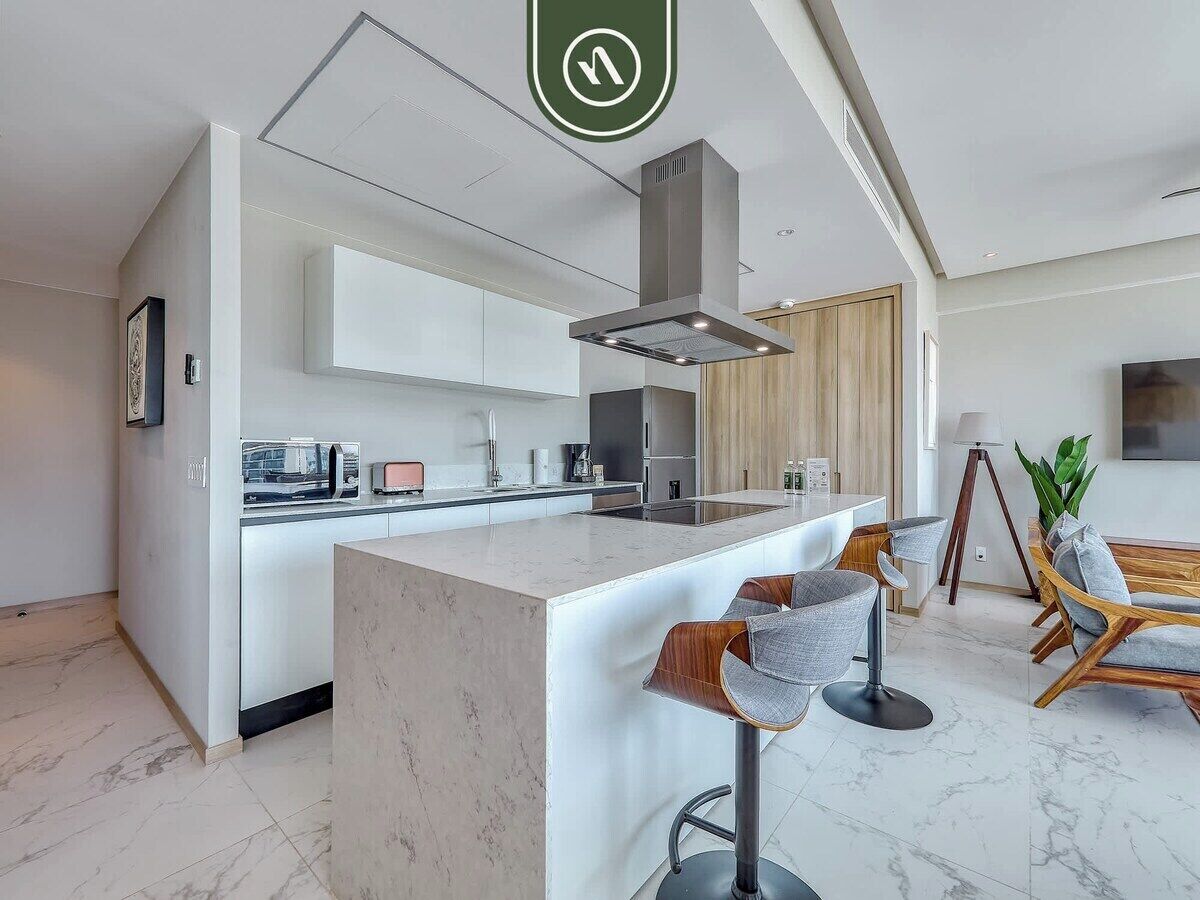 A modern kitchen with a central island, bar stools, and a dining area with wooden chairs.