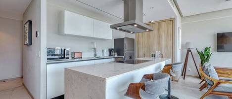 A modern kitchen with a central island, bar stools, and a dining area with wooden chairs.