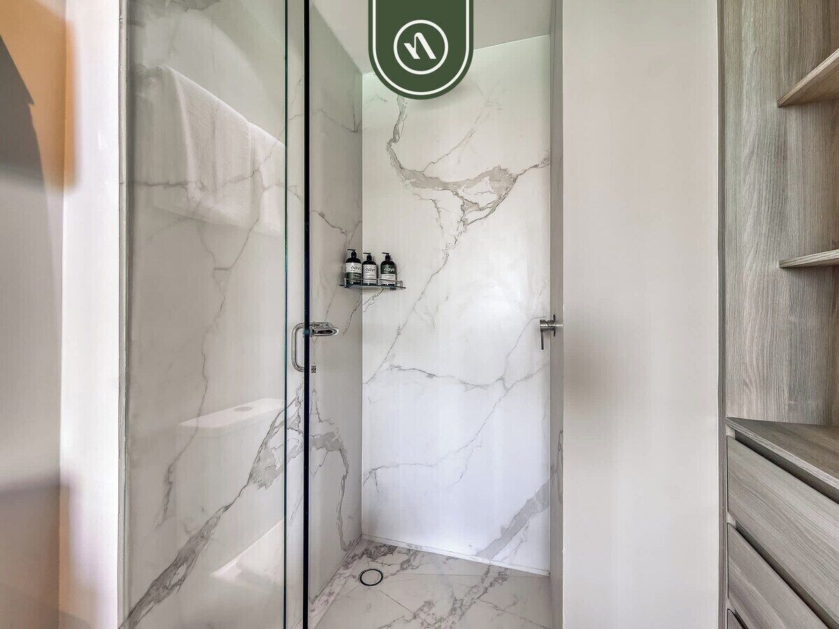 A bathroom with a glass-enclosed shower, marble walls, and a wooden vanity.