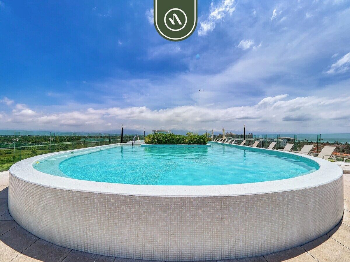 A circular infinity pool with a tiled edge, surrounded by lounge chairs, set against a backdrop of a cloudy sky and distant landscape.