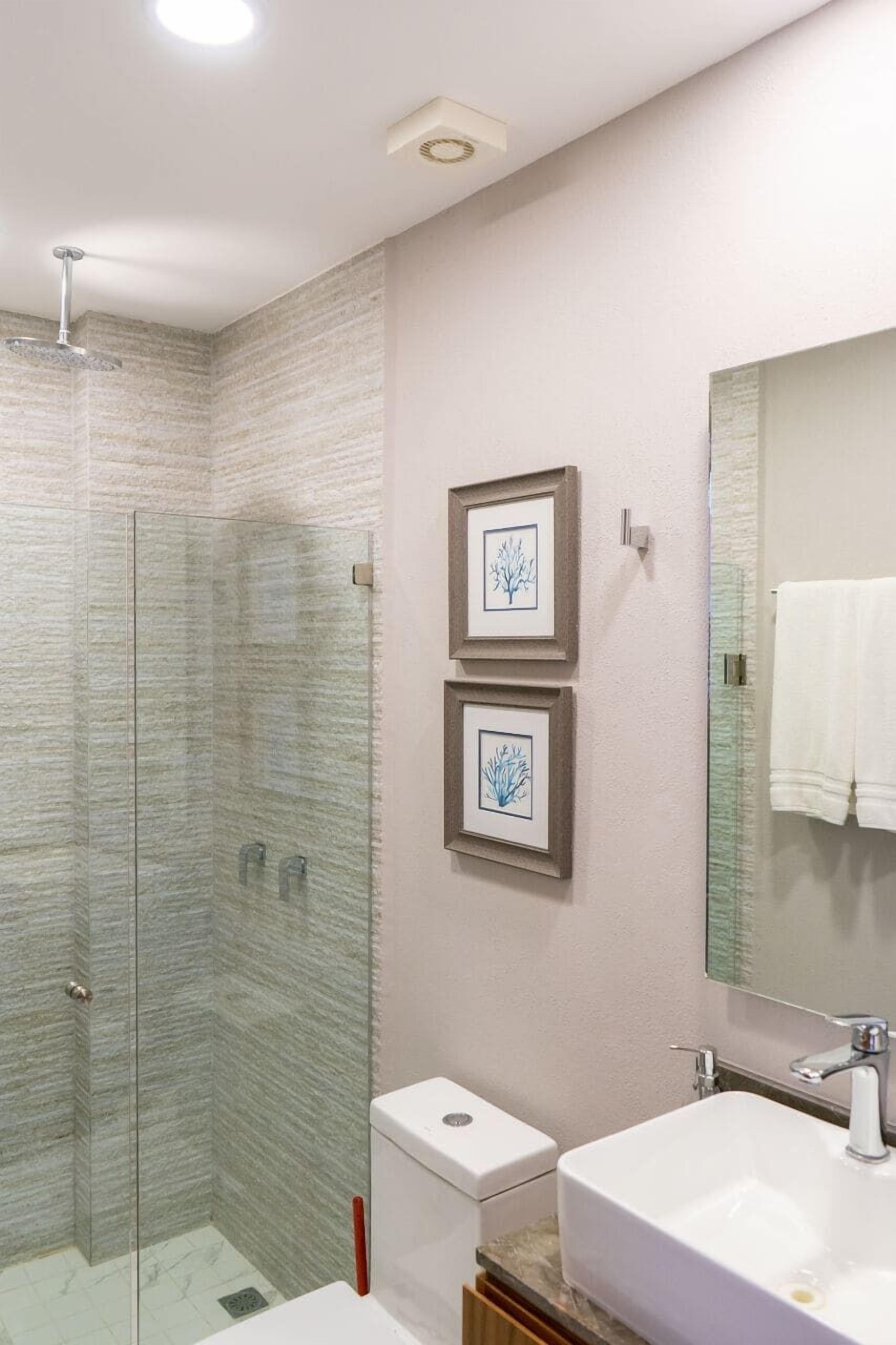 Un baño moderno con ducha de vidrio, inodoro y lavamanos con un espejo grande.