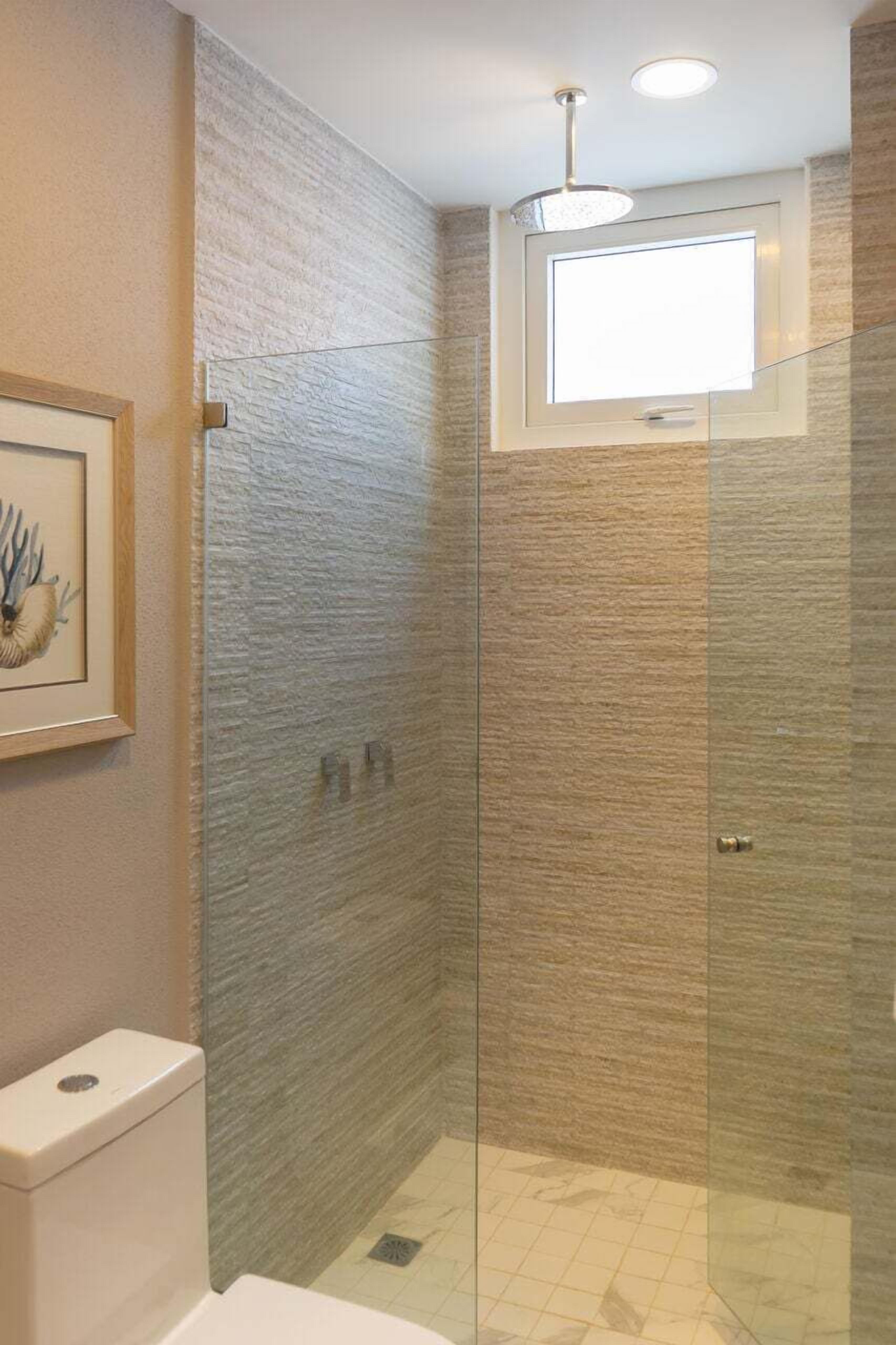 Un baño moderno con cabina de ducha de vidrio, inodoro y un cuadro enmarcado en la pared.