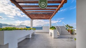 A rooftop terrace with a wooden pergola, white planters with greenery, and a view of the cityscape. - Equipped 2BR Condo in Versalles - Pool - King Bed (Puerto Vallarta)