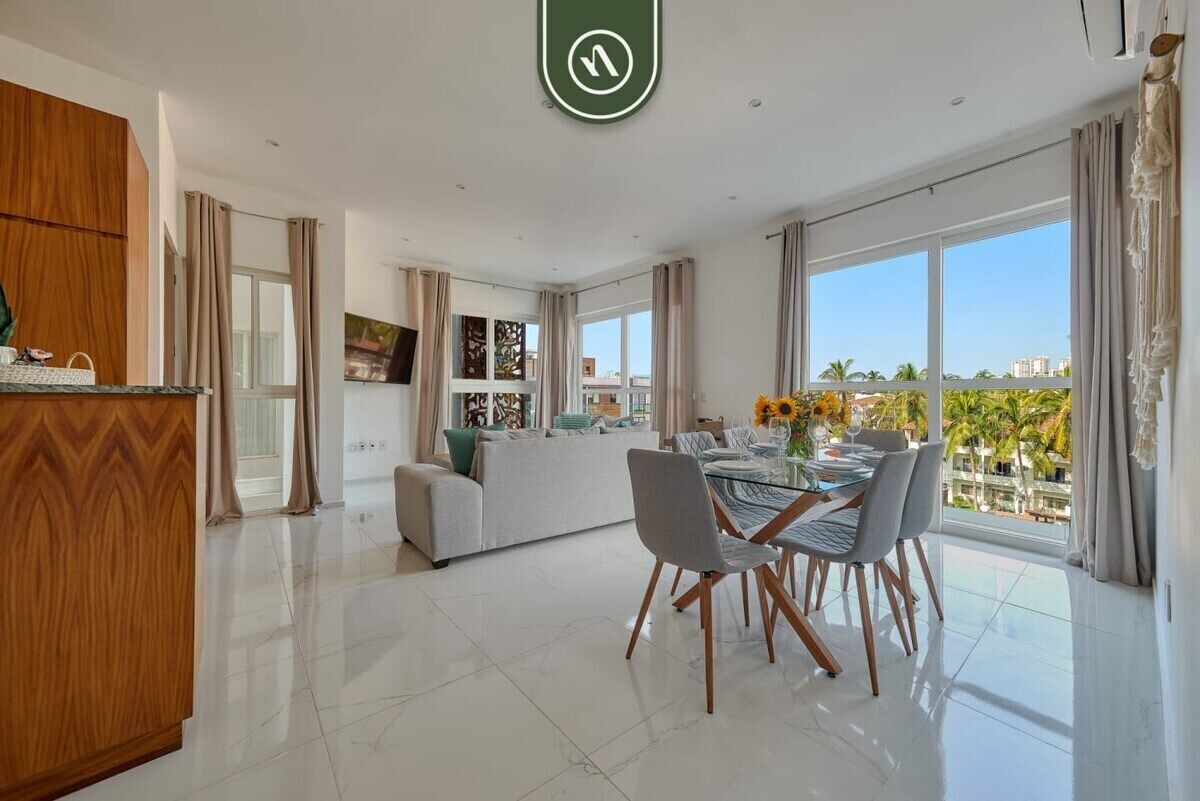 A modern living room with a dining area, large windows, and a view of palm trees.