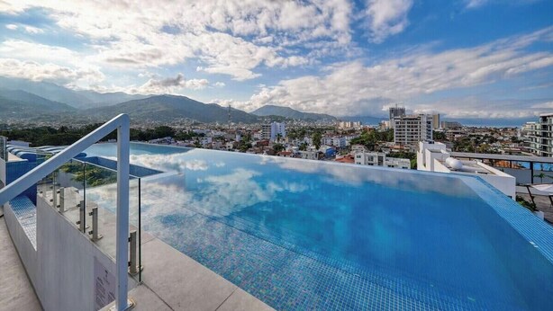 A rooftop infinity pool with a cityscape and mountains in the background. - Equipped 2BR Condo in Versalles - Pool - King Bed (Puerto Vallarta)