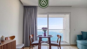 A room with a dining table, chairs, a sofa, a view of the sea, and a balcony door. - Oceanview Studio - King Bed - Pools - Beachclub (Puerto Vallarta)
