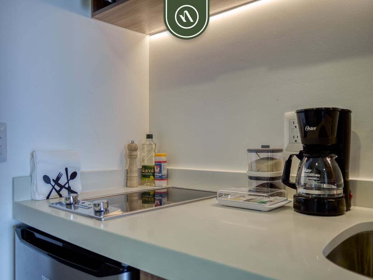 Una kitchenette con cafetera, una botella de agua, un bote de Nutrol y una bandeja con cubiertos.