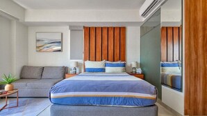 Ein modernes Schlafzimmer mit einem großen Bett, einer Couch, einem kleinen Tisch mit Pflanze und einer Wand-Klimaanlage.