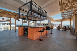 A spacious outdoor bar area with a high ceiling, a central bar counter, and multiple seating options.