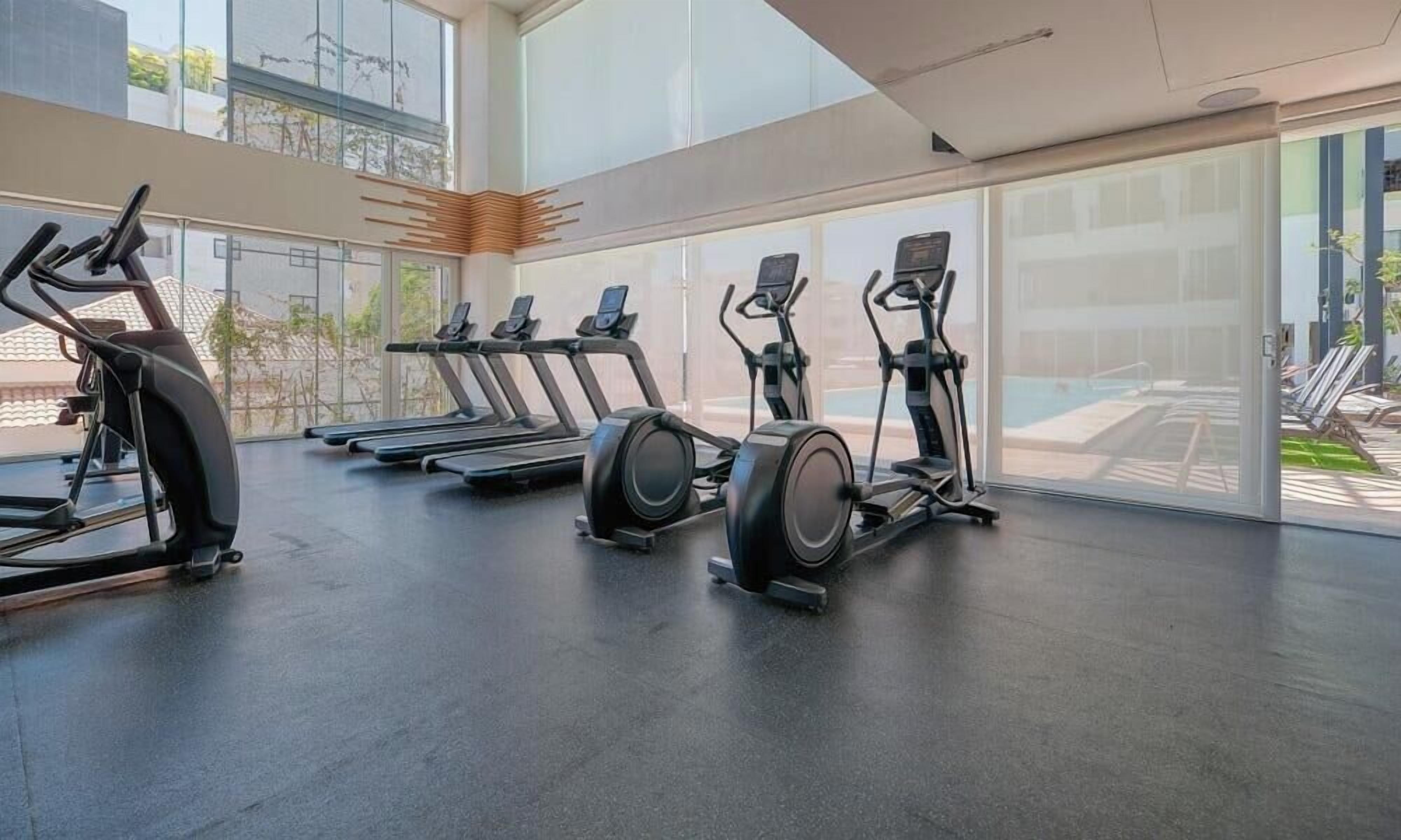 A gym with treadmills, elliptical machines, and a large glass window.