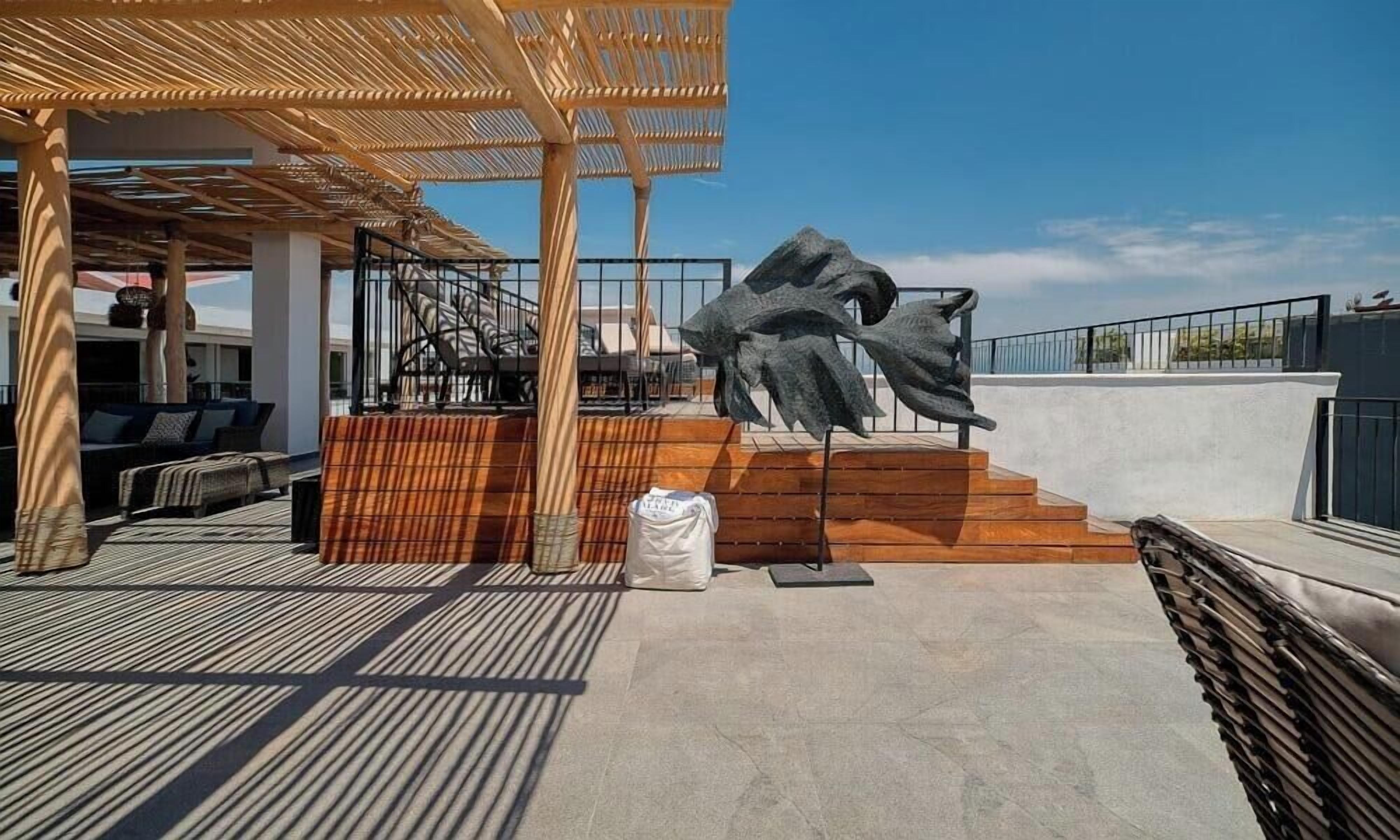 Une terrasse sur le toit agrémentée d’une pergola en bois, d’une grande sculpture abstraite et d’un espace détente avec des coussins.