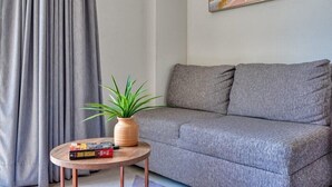 Ein graues Sofa, ein runder Holztisch mit Pflanze und Büchern sowie ein Bild an der Wand.