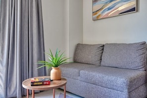 Un sofá gris, una mesa redonda de madera con una planta y libros, y un cuadro en la pared.