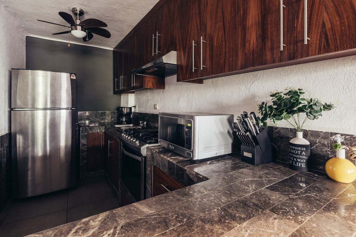 A modern kitchen with dark wood cabinets, stainless steel appliances, and a marble countertop.