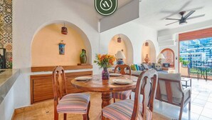 A dining area with a round wooden table, striped upholstered chairs, and a view of the city through large windows. - Ocean View 1Br Condo-balcony-beach-pool - 606 (Puerto Vallarta)