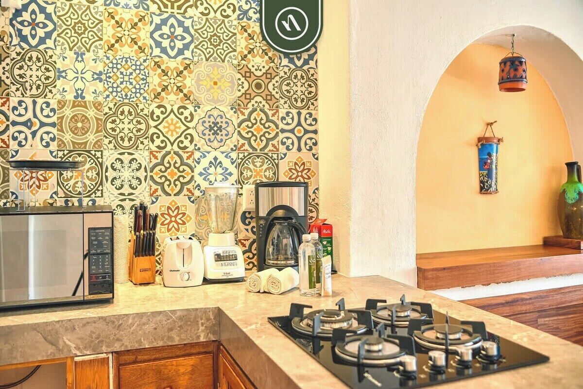 Une cuisine avec un crédence carrelée à motifs, un four à micro-ondes, un grille-pain, un mixeur, une machine à café et une cuisinière à gaz.