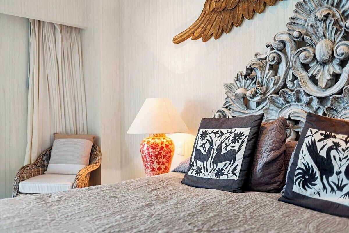 Un lit avec une literie à motifs, une lampe, des coussins décoratifs, une chaise et un mur orné de motifs.