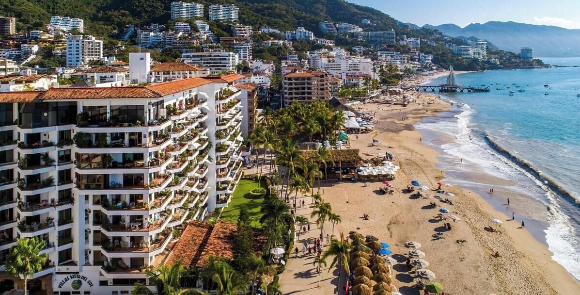 A coastal hotel with multiple balconies, a beach, and a pier.