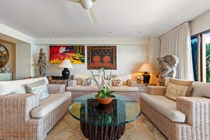 Un salon moderne avec des meubles en osier, une table basse en verre et des œuvres d’art accrochées aux murs.