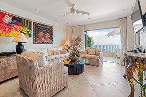 A spacious living room with wicker furniture, a ceiling fan, and a large window with a view. - Ocean View 2Br Condo-balcony-beach-pool - 712 (Puerto Vallarta)