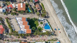 Vista aérea de un complejo turístico costero con múltiples piscinas, una playa y palmeras.