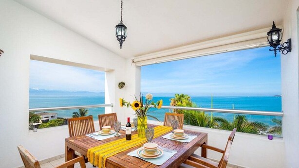 Un comedor con una mesa y sillas de madera, un camino de mesa amarillo y un jarrón con girasoles.