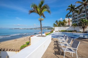 A poolside area with lounge chairs, a palm tree, and a view of the beach and ocean. - Colibrí Condominiums Colibri 504 (Bucerías)