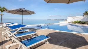 Zona de piscina con sillones de descanso y sombrillas, con vistas a una masa de agua.